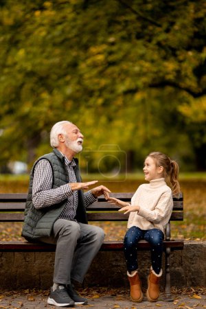 Téléchargez les photos : Beau grand-père jouant aux mains rouges gifle jeu avec sa petite-fille dans le parc le jour de l'automne - en image libre de droit