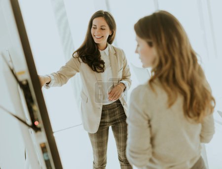 Téléchargez les photos : Deux jeunes femmes d'affaires discutent des résultats financiers sur le grand écran mural du bureau - en image libre de droit