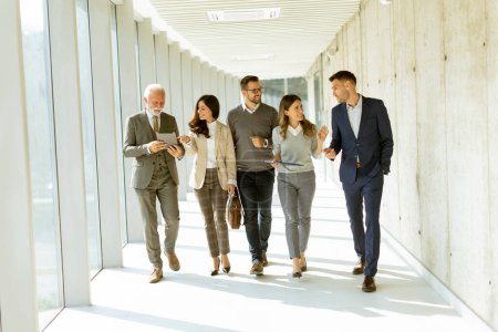 Téléchargez les photos : Groupe de professionnels des entreprises marchant dans le couloir du bureau par une journée ensoleillée - en image libre de droit