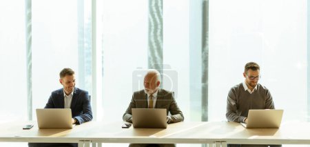 Téléchargez les photos : Homme d'affaires senior et les jeunes hommes d'affaires travaillant ensemble sur les ordinateurs portables dans le bureau - en image libre de droit