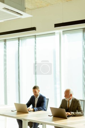 Téléchargez les photos : Senior et les jeunes hommes d'affaires travaillant ensemble sur les ordinateurs portables dans le bureau - en image libre de droit