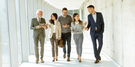 Photo for Group of corporate business professionals walking through office corridor on a sunny day - Royalty Free Image
