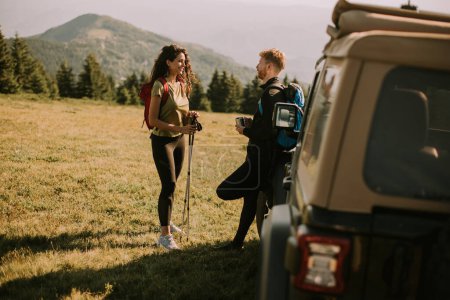 Téléchargez les photos : Smiling young couple preparing hiking adventure with backpacks by terrain vehicle - en image libre de droit