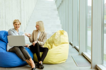 Téléchargez les photos : Deux femmes d'affaires travaillant sur ordinateur portable sur des sacs paresseux dans le bureau moderne - en image libre de droit