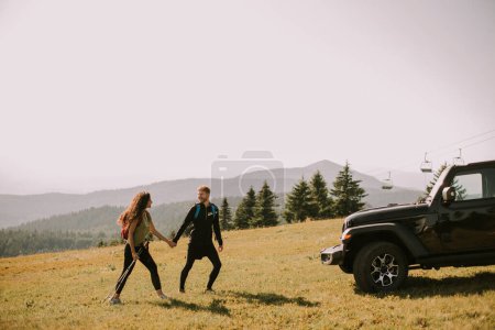 Téléchargez les photos : Jeune couple souriant marchant avec des sacs à dos sur les collines verdoyantes - en image libre de droit