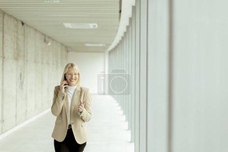 Foto de Empresaria usando teléfono móvil mientras está de pie en el moderno pasillo de la oficina - Imagen libre de derechos