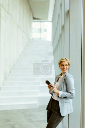 Photo for Businesswoman using mobile phone while standing on the modern office hallway - Royalty Free Image