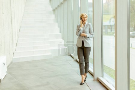 Téléchargez les photos : Femme d'affaires utilisant un téléphone portable tout en se tenant sur le couloir de bureau moderne - en image libre de droit