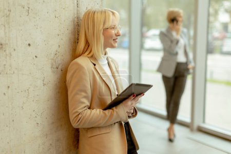 Téléchargez les photos : Deux femmes d'affaires debout avec ordinateur portable et téléphone portable dans le couloir du bureau - en image libre de droit