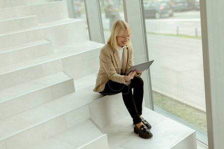 Téléchargez les photos : Femme d'affaires travaillant sur tablette numérique sur les escaliers de bureau modernes - en image libre de droit
