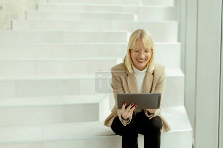 Téléchargez les photos : Femme d'affaires travaillant sur tablette numérique sur les escaliers de bureau modernes - en image libre de droit