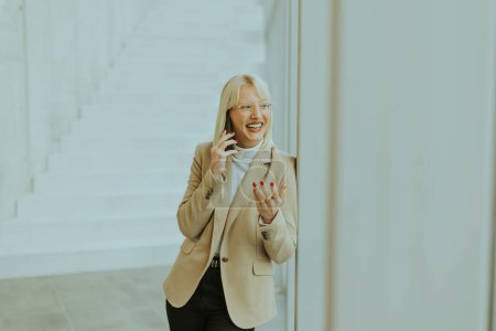 Téléchargez les photos : Femme d'affaires utilisant un téléphone portable tout en se tenant sur le couloir de bureau moderne - en image libre de droit