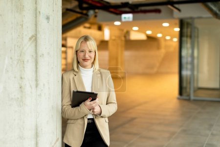 Téléchargez les photos : Femme d'affaires avec tablette numérique sur le couloir de bureau moderne - en image libre de droit