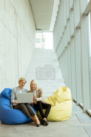 Foto de Dos mujeres de negocios que trabajan en el ordenador portátil en bolsas perezosas en la oficina moderna - Imagen libre de derechos