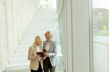 Photo for Two business women walking with laptop and mobile phone in the office corridor - Royalty Free Image