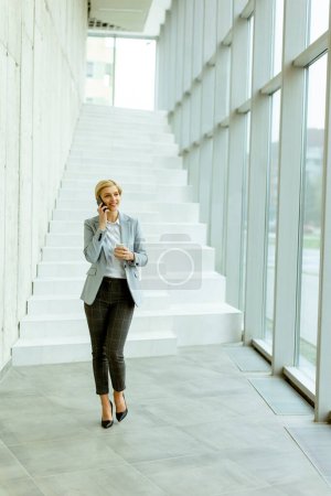Photo for Businesswoman using mobile phone while walking on the modern office hallway - Royalty Free Image