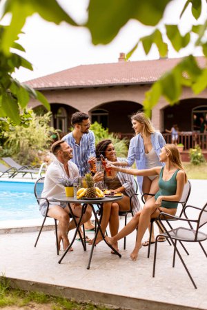 Photo for Group of happy young people cheering with cider by the pool in the garden - Royalty Free Image