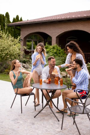 Photo for Group of happy young people cheering with cider and eating pizza by the pool in the garden - Royalty Free Image