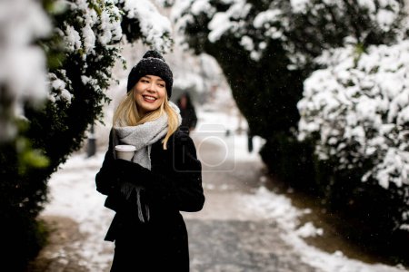 Foto de Pretty young woman in warm clothes enjoying in snow with takeaway coffee cup - Imagen libre de derechos