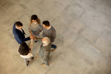 Photo for Group of young and senior business people come together in an office hallway, standing in a circle with their hands joined. They are dressed professionally, reflecting their business acumen and status. Their teamwork and collaboration symbolize the u - Royalty Free Image