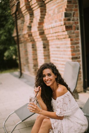 Foto de Pretty young woman with curly hair relaxes on a deck chair and enjoys a glass of fresh lemonade - Imagen libre de derechos