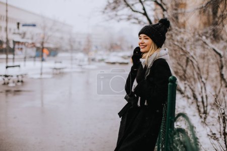 Téléchargez les photos : Pretty young woman in warm clothes using mobile phone on a winter day - en image libre de droit