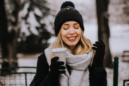Foto de Pretty young woman in warm clothes enjoying in snow with takeaway coffee cup - Imagen libre de derechos