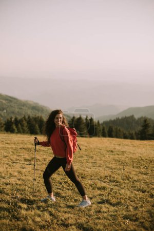Téléchargez les photos : Young woman is taking a scenic hike on a hill, carrying all her necessary gear in a backpack. She appears to be a seasoned hiker, enjoying the challenge and beauty of the outdoor experience - en image libre de droit
