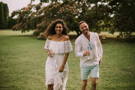 Foto de Happy young couple is enjoying the beautiful surroundings of a garden with glasses of fresh lemonade - Imagen libre de derechos