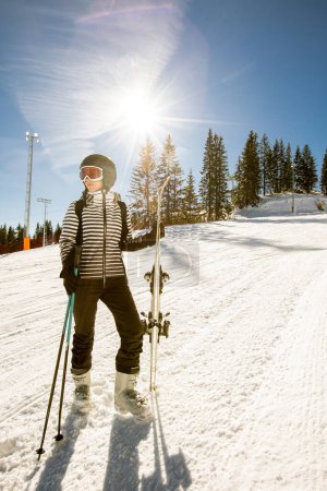 Téléchargez les photos : Une seule jeune femme profite d'une journée ensoleillée de ski d'hiver, vêtue d'un équipement complet de neige avec des bottes de ski et des lunettes de soleil. - en image libre de droit