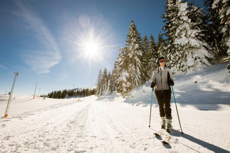 Foto de Una joven soltera disfruta de un soleado día de invierno de esquí, vestida con equipo de nieve completo con botas de esquí y gafas de sol - Imagen libre de derechos