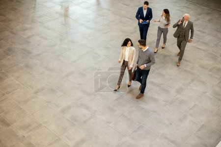Téléchargez les photos : Group of young and senior business people are walking in an office hallway, captured in an aerial view. They are dressed in formal attire, walking with purpose and intent and discussing amongst themselves and interacting with colleagues - en image libre de droit