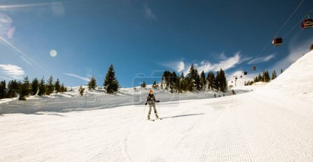 Téléchargez les photos : Une fille célibataire profite d'une journée ensoleillée d'hiver de ski, vêtue d'un équipement complet de neige avec des bottes de ski et des lunettes de soleil - en image libre de droit