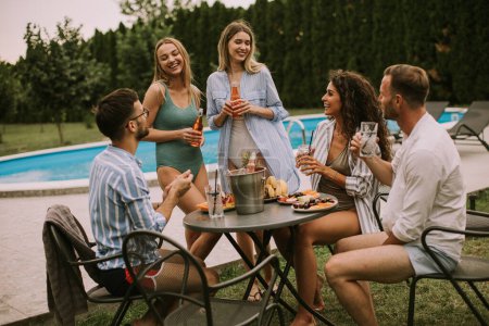 Foto de Group of happy young people cheering with cider by the pool in the garden - Imagen libre de derechos