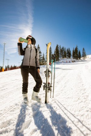 Photo for Young woman enjoying winter day of skiing on the snow covered slopes, surrounded by tall trees and dressed for cold temperatures - Royalty Free Image
