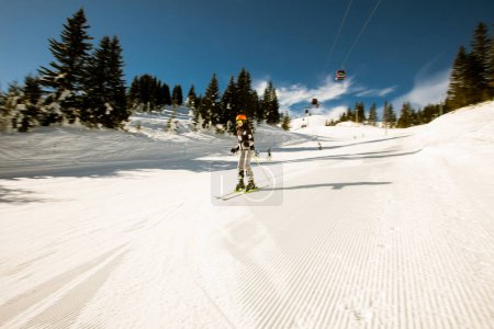 Photo for A single girl enjoys a sunny winter day of skiing, dressed in full snow gear with ski boots and sunglasses - Royalty Free Image