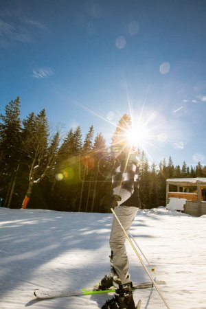 Photo for A single girl enjoys a sunny winter day of skiing, dressed in full snow gear with ski boots and sunglasses - Royalty Free Image