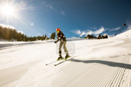Foto de Una chica soltera disfruta de un soleado día de invierno de esquí, vestida con todo el equipo de nieve con botas de esquí y gafas de sol - Imagen libre de derechos