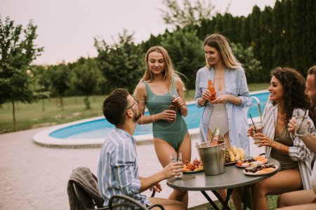 Photo for Group of happy young people cheering with cider by the pool in the garden - Royalty Free Image