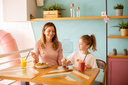 Téléchargez les photos : Mère et fille passer un bon moment pendant le petit déjeuner avec des jus de fruits frais pressés dans le café - en image libre de droit