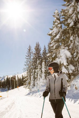 Photo for Young woman enjoying winter day of skiing on the snow covered slopes, surrounded by tall trees and dressed for cold temperatures - Royalty Free Image