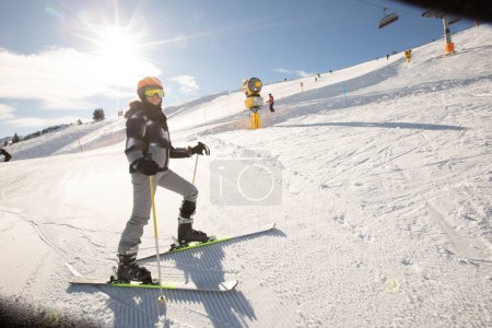 Foto de Una chica soltera disfruta de un soleado día de invierno de esquí, vestida con todo el equipo de nieve con botas de esquí y gafas de sol - Imagen libre de derechos