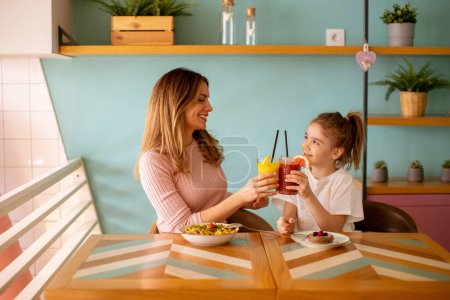 Photo for Mother and daughter having good time during breakfast with fresh squeezed juices in the cafe - Royalty Free Image