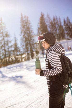 Téléchargez les photos : Jeune femme profitant de la journée hivernale de ski sur les pistes enneigées, entourée de grands arbres et habillée pour le froid - en image libre de droit