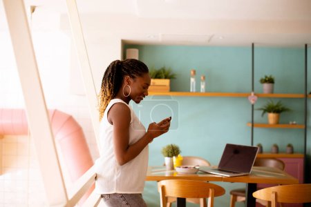 Téléchargez les photos : Jolie jeune femme noire utilisant un téléphone portable dans le café - en image libre de droit