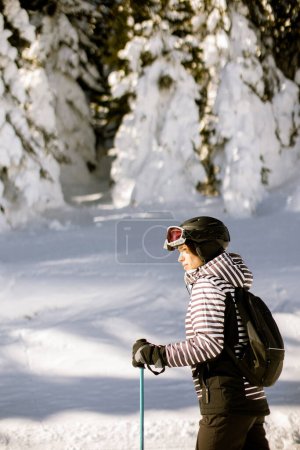 Foto de Joven mujer disfrutando de un día de invierno esquiando en las pistas cubiertas de nieve, rodeada de árboles altos y vestida para temperaturas frías - Imagen libre de derechos