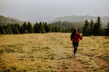 Téléchargez les photos : Jeune femme souriante marchant avec sac à dos sur les collines verdoyantes - en image libre de droit