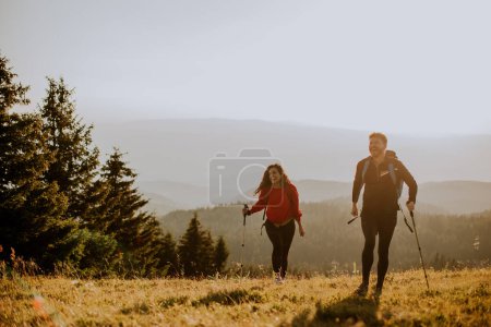 Foto de Sonriente joven pareja caminando con mochilas sobre verdes colinas - Imagen libre de derechos