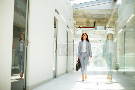 Téléchargez les photos : Jolie jeune femme d'affaires marchant avec mallette dans le couloir du bureau - en image libre de droit