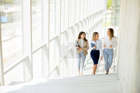 Téléchargez les photos : Trois jolies jeunes femmes d'affaires marchant dans les escaliers dans le couloir du bureau - en image libre de droit